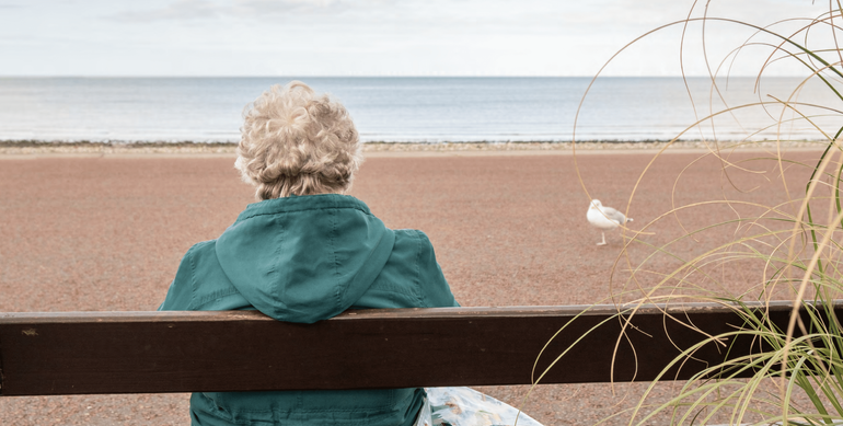 Photo d'une personne âgée seule assise sur un banc regardant la mer